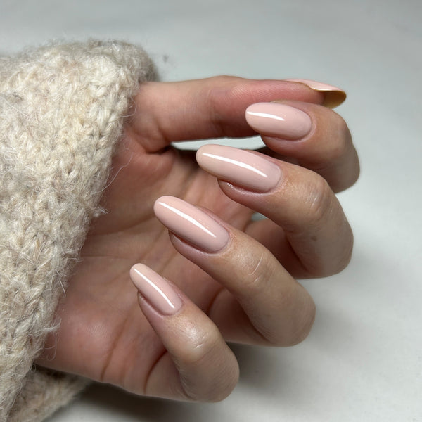 Hand with creamy tauoe nail gel wearing a beige knit sleeve on a neutral background