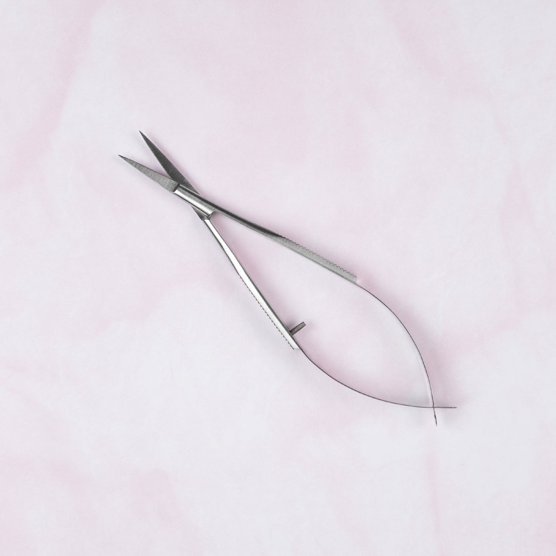 Pair of silver cuticle scissors on a light pink background