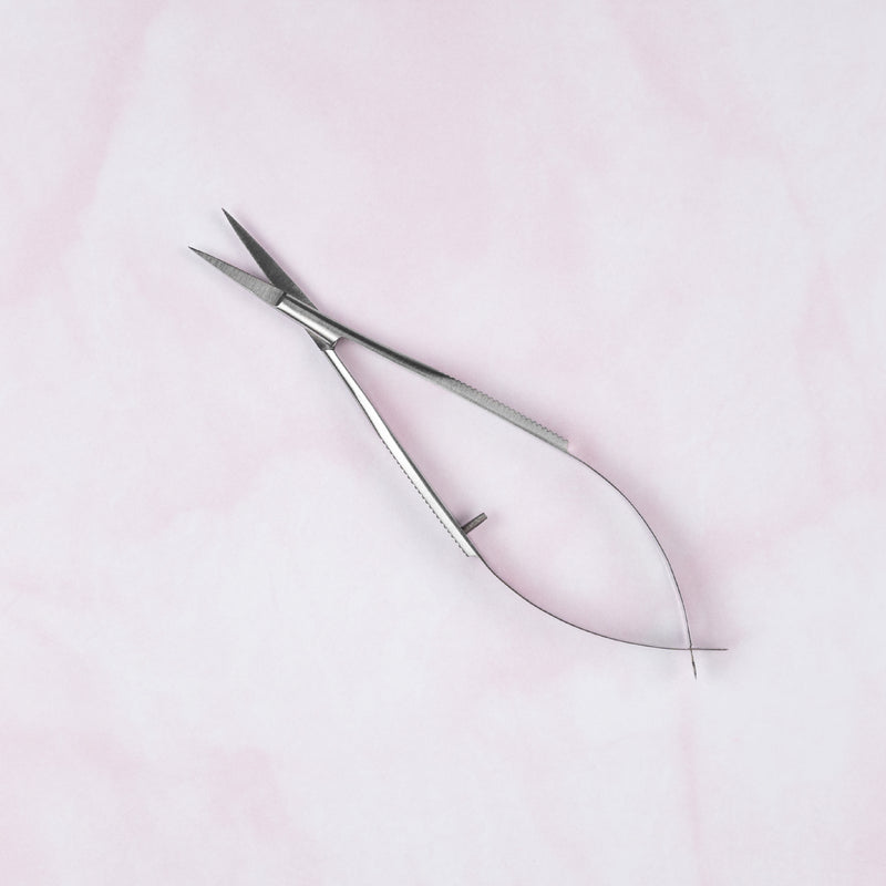 Pair of silver cuticle scissors on a light pink background