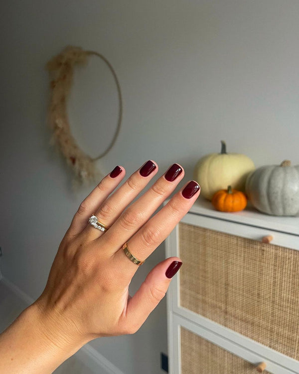 Hand with Mulled Wine Calgel, a deep red nail gel with pumps in background