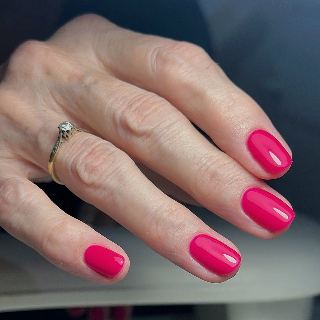 Hand with raspberry nail gelwearing a gold ring on a blurred background in Calgel Raspberry Gloss.